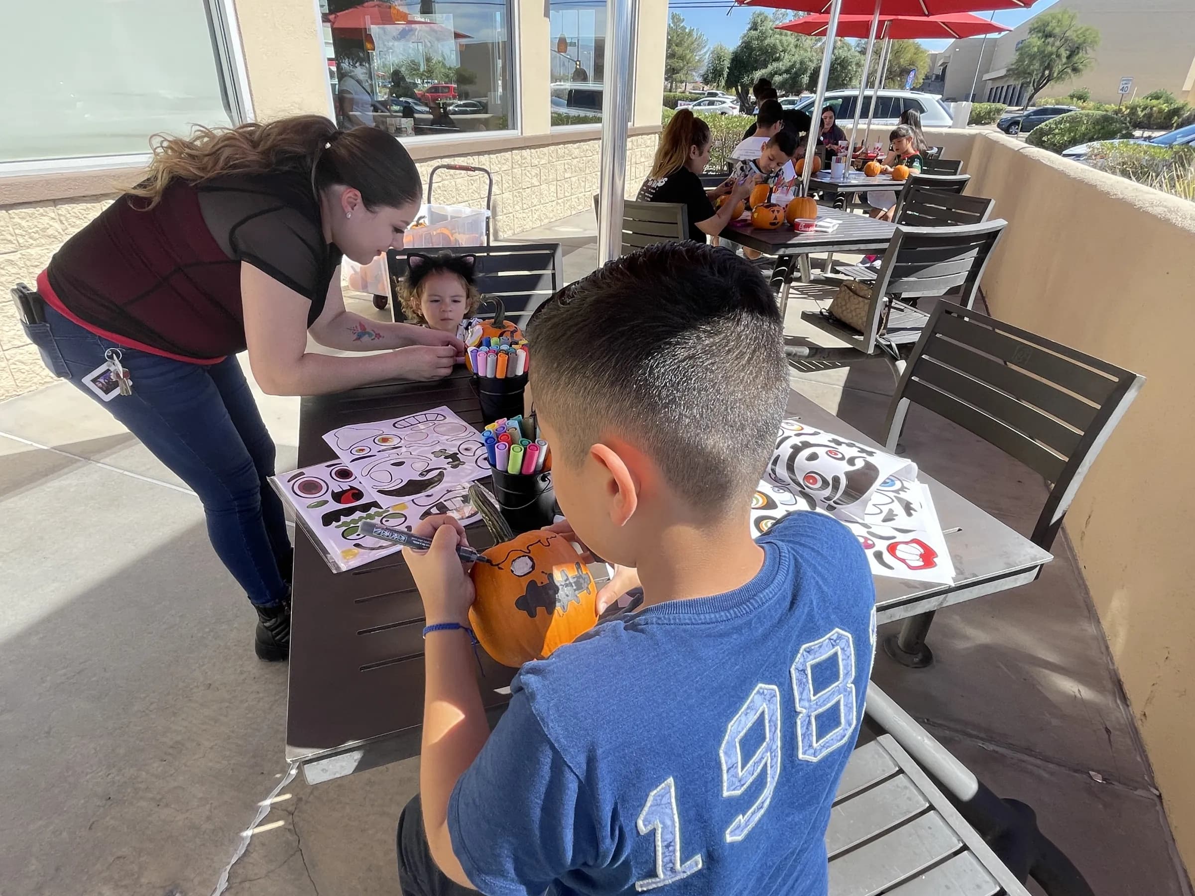 Children painting pumpkins with a volunteer at an outdoor fall event